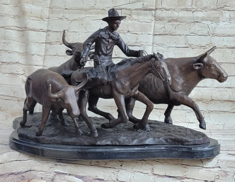 Bronze figurine of a cowboy riding among cattle on a dark base